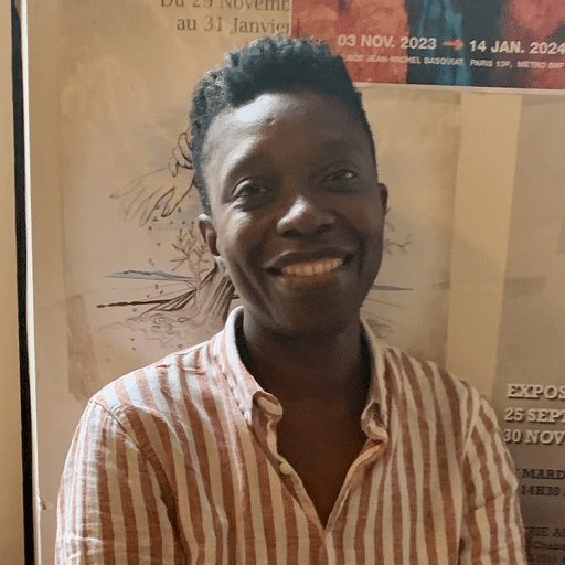 A smiling person in a striped shirt standing in front of posters.