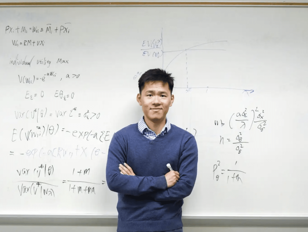 A person in a blue sweater stands in front of a whiteboard covered with complex mathematical equations.