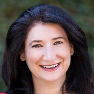 A smiling woman with dark hair outdoors.