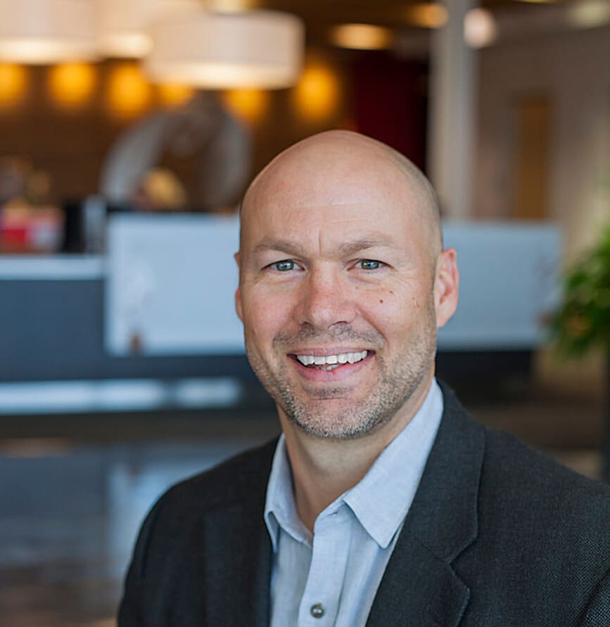 Smiling bald man in a dark blazer in a modern office lobby.